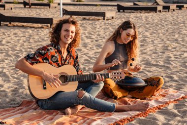 Genç ve mutlu bir çiftin plajda gitar ve davul çalması.