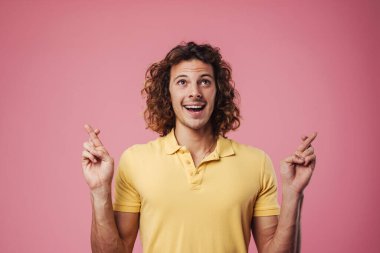 İyi şans dilemek için dua eden yakışıklı beyaz adam pembe arka planda izole edilmiş.