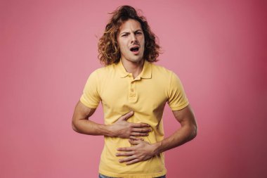 Mutsuz yakışıklı adam poz veriyor ve karnını okşuyor. Pembe arka planda izole edilmiş.