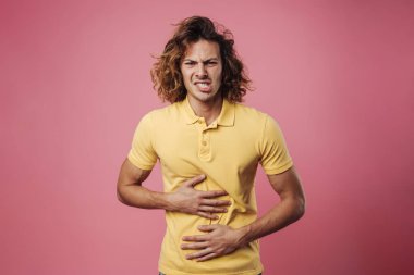 Mutsuz yakışıklı adam poz veriyor ve karnını okşuyor. Pembe arka planda izole edilmiş.