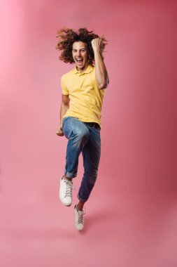 Heyecanlı yakışıklı adam pembe arka planda tek başına atlarken kazanan hareketi yapıyor.