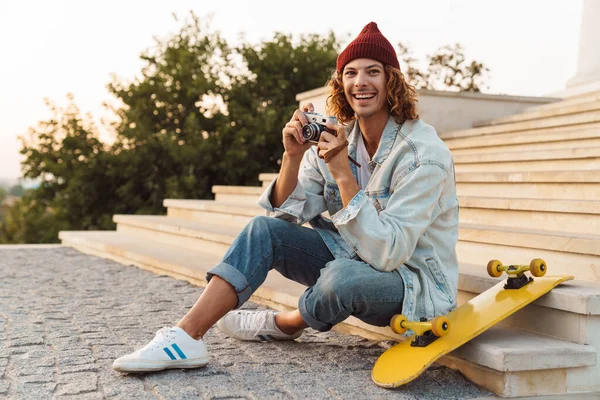 Foto Van Positieve Jonge Krullende Man Scater Zittend Buiten Met — Stockfoto