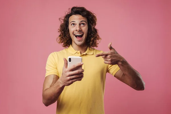 快乐英俊的男人拿着手机指指点点用粉红背景隔开的手机 — 图库照片