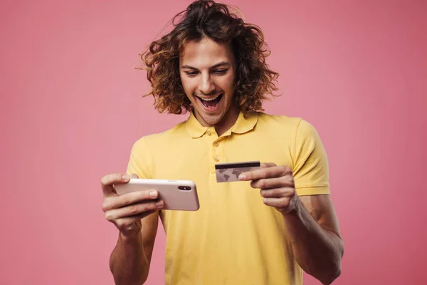 Glädjande Snygg Kille Poserar Med Kreditkort Och Mobiltelefon Isolerad Över — Stockfoto