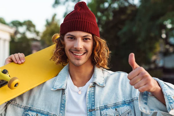 Fotografie Šťastného Veselý Mladý Kudrnatý Muž Kráčející Venku Ulici Skateboard — Stock fotografie