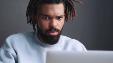 Yakışıklı, Afro-Amerikan bir adam evdeki masada dizüstü bilgisayarını kullanıyor.