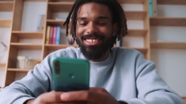 Mutlu, Afro-Amerikan bir adam akıllı telefonunu masada otururken kullanıyor.