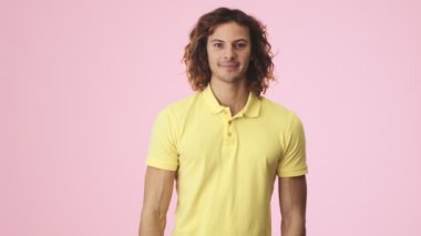 Pozitif kıvırcık bir genç iyi bir jest yapıyor. Stüdyoda pembe bir arka planda tek başına duruyor.