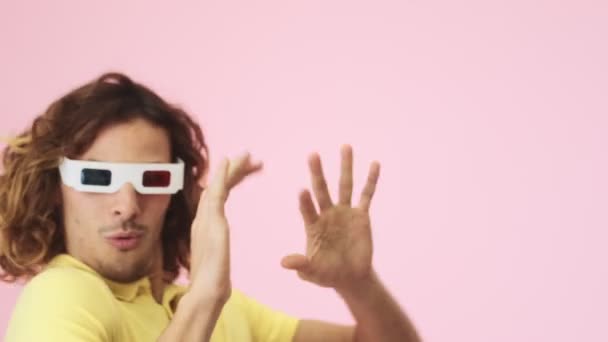 一位情绪激动 卷曲的年轻人 带着3D眼镜 一边看着电影 一边在工作室的粉红背景上与外界隔绝 — 图库视频影像