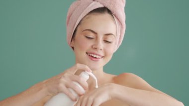 Kafasında havlu olan güzel bir kadın stüdyoda mavi arka planda tek başına duran vücut losyonunu sürüyor.