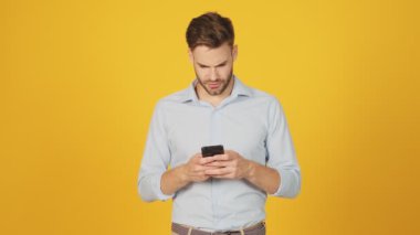 Canı sıkkın genç bir adam akıllı telefonunu stüdyodaki sarı arka planda duruyor.