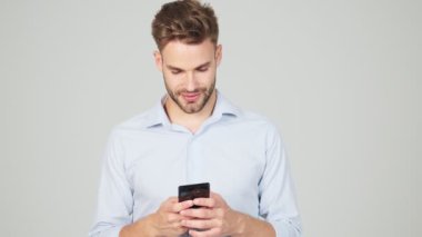 Çekici genç bir işadamı, stüdyodaki gri arka planda duran akıllı telefonunu kullanarak sohbet ediyor.