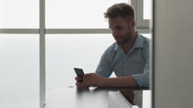 Odaklanmış genç bir işadamı akıllı telefonunu evde otururken kullanıyor.