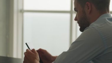 Dikiz ayarı odaklı genç bir işadamı akıllı telefonunu evde mutfakta otururken kullanıyor.