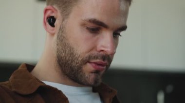 Kulaklıklı, odaklanmış genç bir adamın yakın çekim görüntüsü evde oturan bilgisayarla çalışıyor.