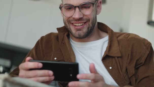 Ένας Χαρούμενος Νέος Που Φοράει Γυαλιά Χρησιμοποιεί Smartphone Του Καθισμένος — Αρχείο Βίντεο