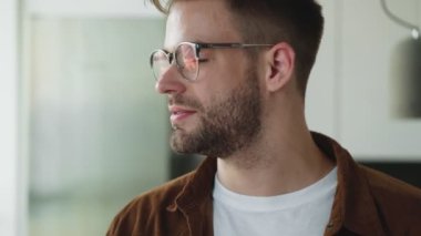Gülümseyen genç bir adam gözlüğünü evde otururken çıkarıyor.