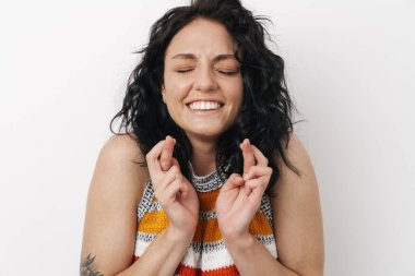 Beyaz duvar arkasında izole edilmiş güzel, genç bir kadın umut dolu parmaklarını çapraz gösteriyor.