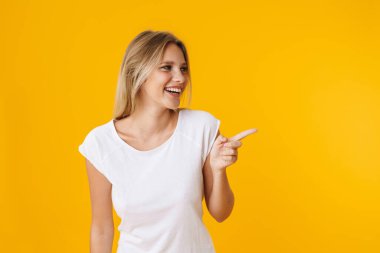 Neşeli güzel kız gülümserken sarı arka planda izole edilmiş bir şekilde parmağıyla işaret ediyor.