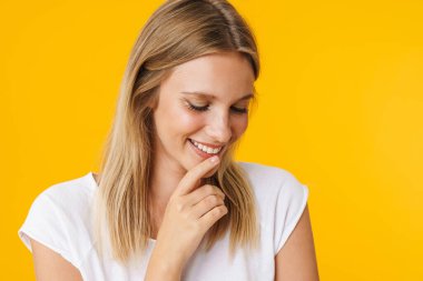 Gülümseyen ve aşağıya bakan neşeli güzel kız sarı arka planda izole edilmiş.