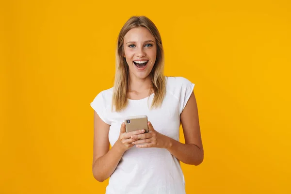 Spännande Blond Flicka Ler Och Använder Mobiltelefon Isolerad Över Gul — Stockfoto