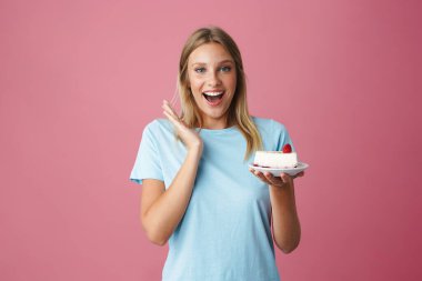 Heyecanlı güzel kız, pembe arka planda izole edilmiş doğum günü pastasıyla poz veriyor.