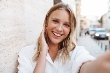 Güzel mutlu kadın gülümsüyor ve şehirde yürürken selfie çekiyor.