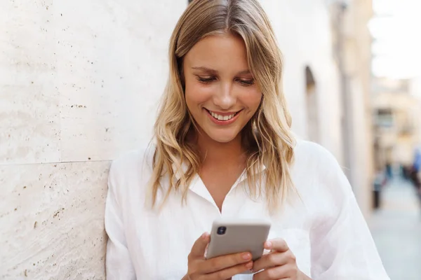 Счастливая Женщина Улыбается Пользуется Мобильным Телефоном Опираясь Стену Городской Улице — стоковое фото