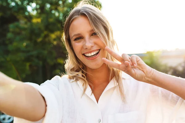 Piękna Szczęśliwa Kobieta Gestykulując Znak Pokoju Robiąc Selfie Podczas Spaceru — Zdjęcie stockowe