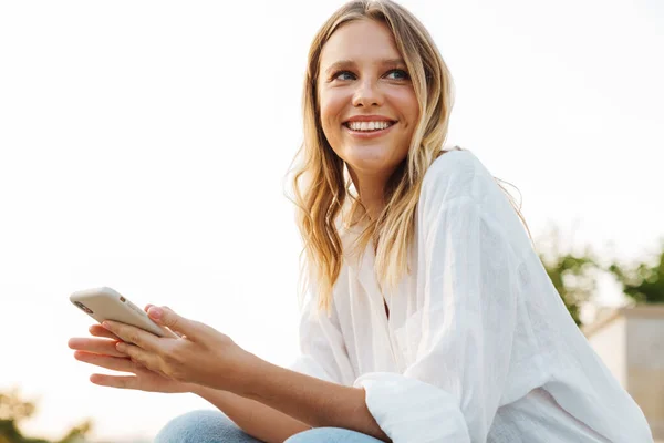 Miła Szczęśliwa Kobieta Uśmiechnięta Korzystająca Telefonu Komórkowego Podczas Siedzenia Zewnątrz — Zdjęcie stockowe