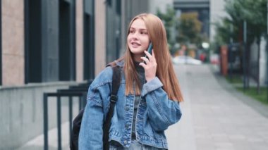 Güzel bir genç kadın şehirde yürürken akıllı telefonuyla konuşuyor.