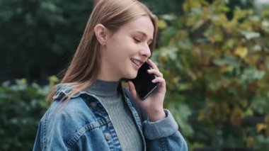 Mutlu genç bir kadın akıllı telefonuyla konuşuyor. Dışarıda, şehirde yürüyor.