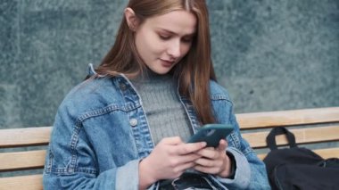 Pozitif bir genç kadın akıllı telefonunu şehrin dışındaki bankta oturuyor.