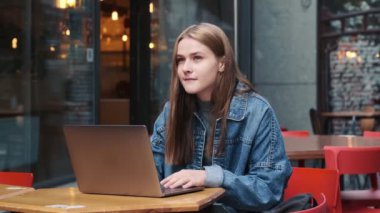 Güzel genç bir kadın şehir kafesinde otururken dizüstü bilgisayarını kullanıyor.