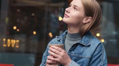 Güzel genç bir kadın, şehirdeki kafede kağıt bardakta sıcak bir içecek tutuyor.