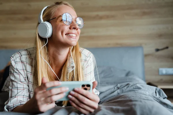 Mujer Rubia Sonriente Escuchando Música Con Auriculares Teléfono Móvil Cama —  Fotos de Stock