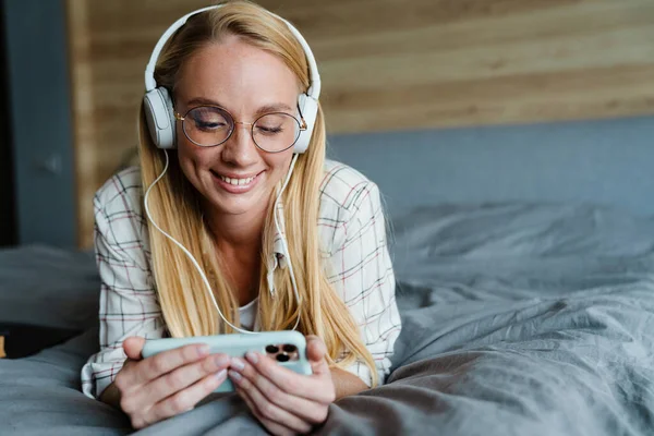 Mujer Rubia Sonriente Escuchando Música Con Auriculares Teléfono Móvil Cama —  Fotos de Stock