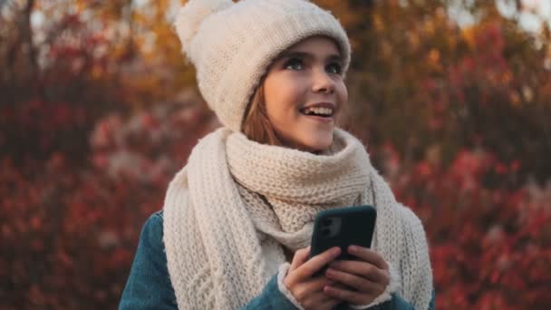 Uśmiechnięta Młoda Dziewczyna Używa Swojego Smartfona Rozglądając Się Parku Zewnątrz — Wideo stockowe