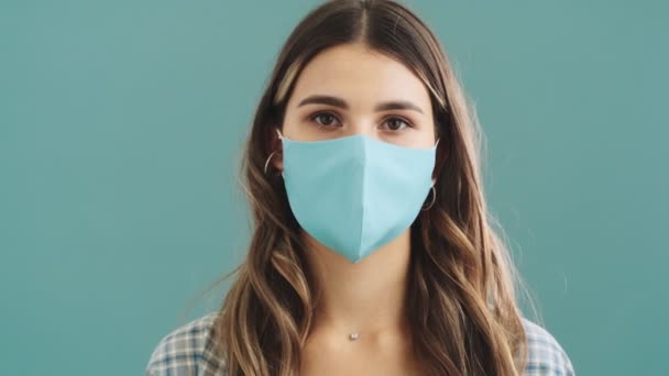 青い背景の上に孤立した をジェスチャーを示している医療保護マスクを身に着けている幸せな女性のクローズアップビュー — ストック動画