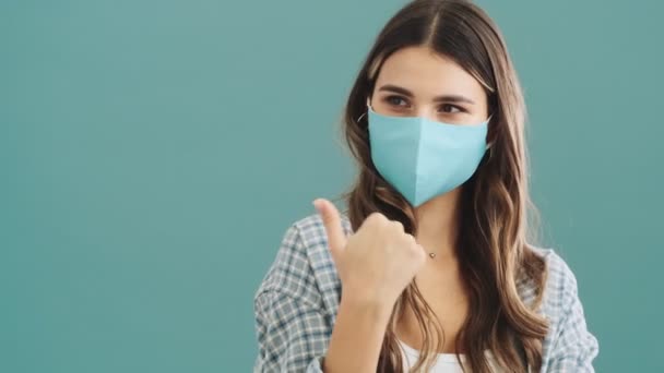 一个戴着医疗防护面具的漂亮女人指着被蓝色背景隔离的一边 — 图库视频影像