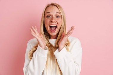 Heyecanlı güzel kız ellerini kaldırıp pembe arka planda gizlenmiş bir şekilde şaşkınlığını ifade ediyor.