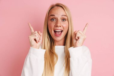 Heyecanlı, güzel bir kız, pembe arka planda dışlanmış parmaklarını havaya kaldırıyor.