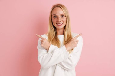 Mutlu güzel kız gülümsüyor ve pembe arka planda izole edilmiş zıt yönleri işaret ediyor.