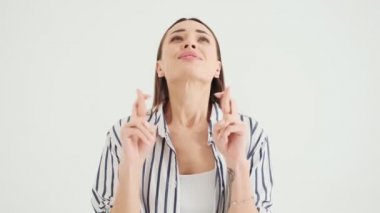 Gülümseyen bir kadın, stüdyoda beyaz arka planda tek başına dikilirken dilek diliyor.