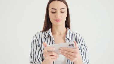 Mutlu bir kadın akıllı telefonunu kullanarak oyun oynuyor. Stüdyoda beyaz arka planda izole bir şekilde duruyor.