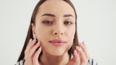 Çekici bir kadın kameraya bakıyor. Stüdyonun beyaz arka planında tek başına duran aynaya bakıyor.