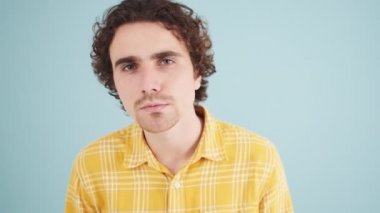 Çekici bir adam kameraya bakıyor. Stüdyodaki mavi duvarın üzerinde duran aynaya bakıyor.