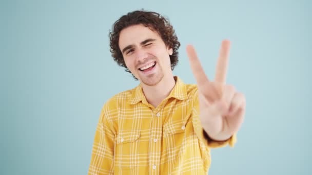 Een Glimlachende Man Toont Een Vredesgebaar Geïsoleerd Boven Blauwe Muur — Stockvideo