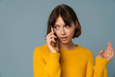 Mavi arka planda izole bir şekilde telefonla konuşan düşünceli bir kadının portresi.