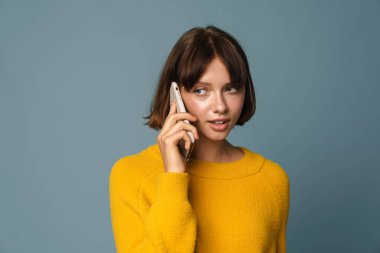 Mavi arka planda izole bir şekilde telefonla konuşan düşünceli bir kadının portresi.